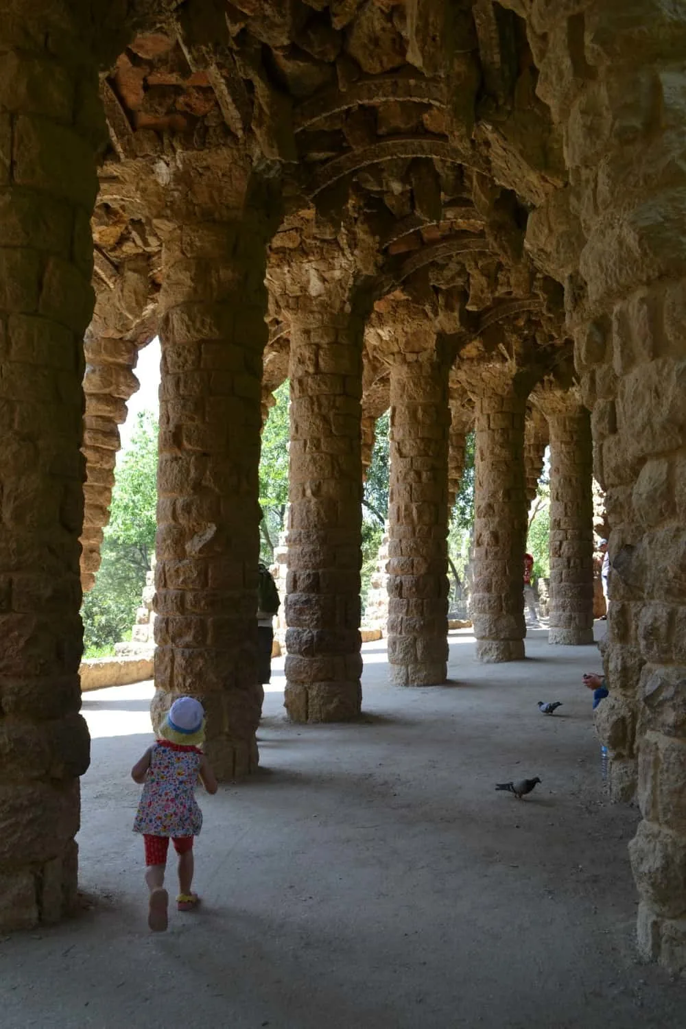 Tin Box Tot walking through arches in Park Guell - Barcelona with a buggy