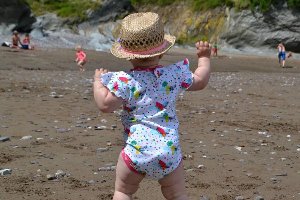 Tin Box Baby walking on the beach in her Rockin' Baby romper suit