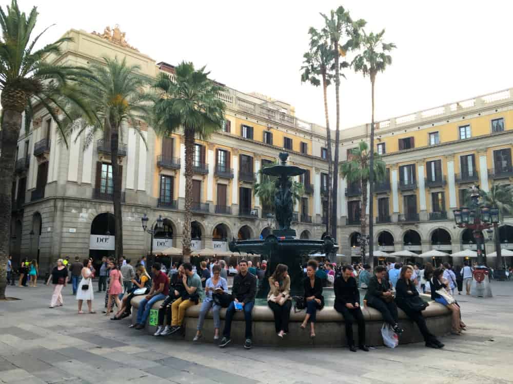 Tourists sitting around a fountain in Placa de Relat - Barcelona with a buggy