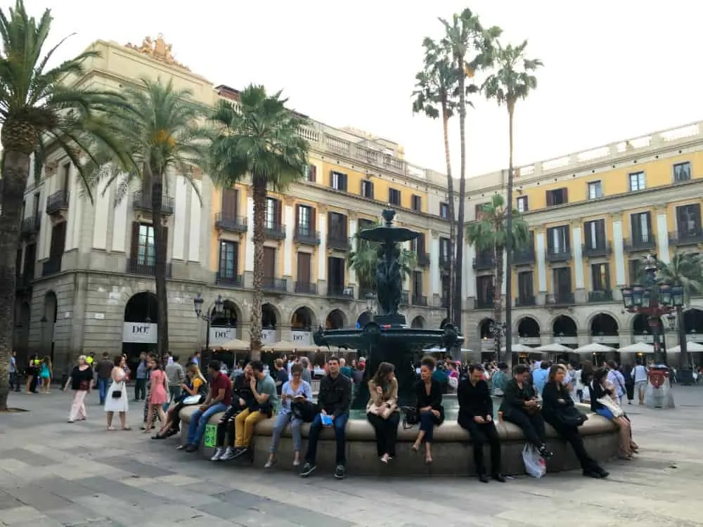 Tourists sitting around a fountain in Placa de Relat - Barcelona with a buggy