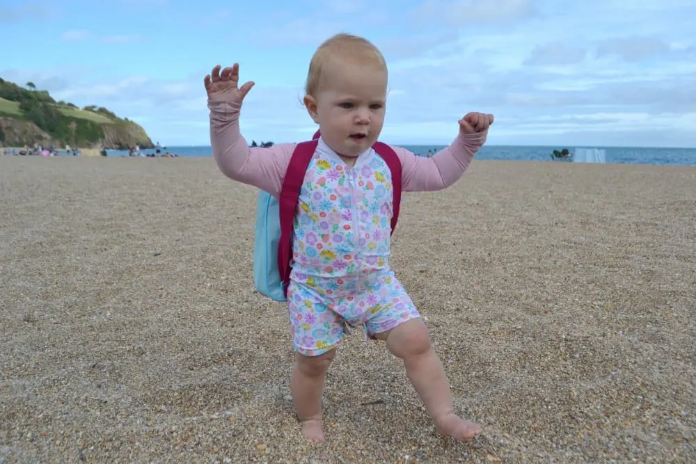 Tin Box Baby walking on beach wearing Platypus swimsuit