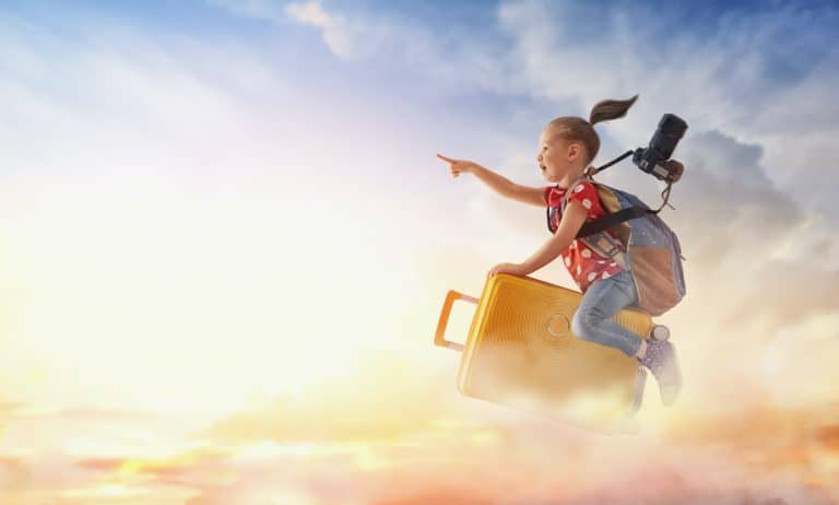 Dreams of travel! Child flying on a suitcase against the backdrop of sunset.