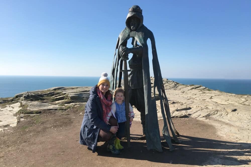 Tin Box Traveller and Baby with the statue at Tintagel Castle in Cornwall