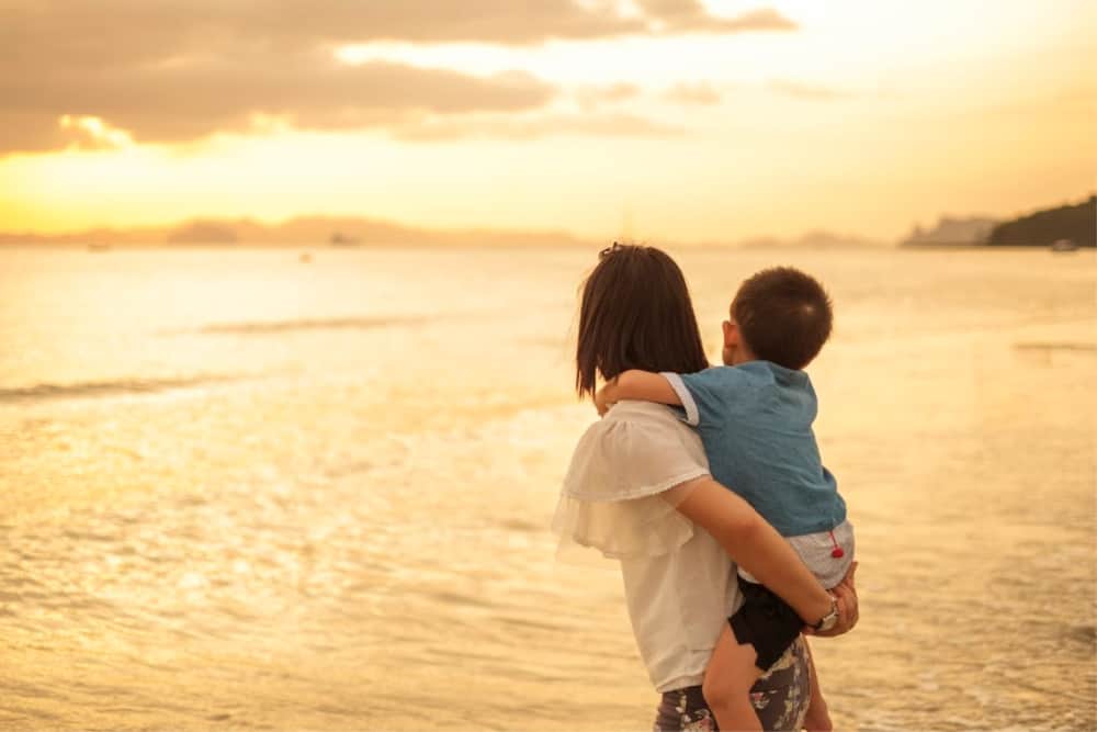 A mother and son on the beach and sea outdoors at sunset - best travel insurance for traveling with children