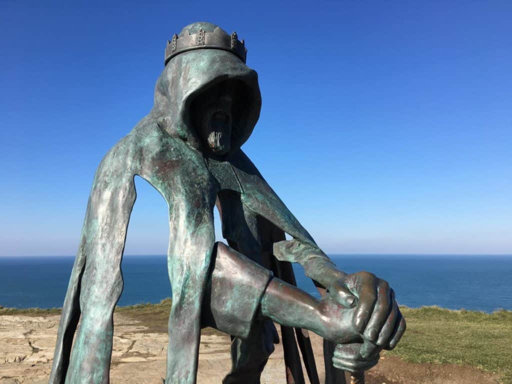 King Arthur's bronze statue at Tintagel Castle with blue sky background
