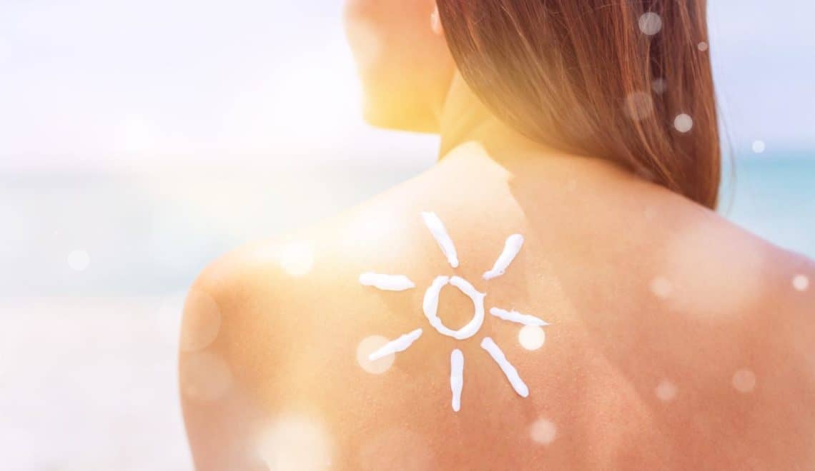 Woman with Sun Cream on her back over ocean background - holiday toiletries