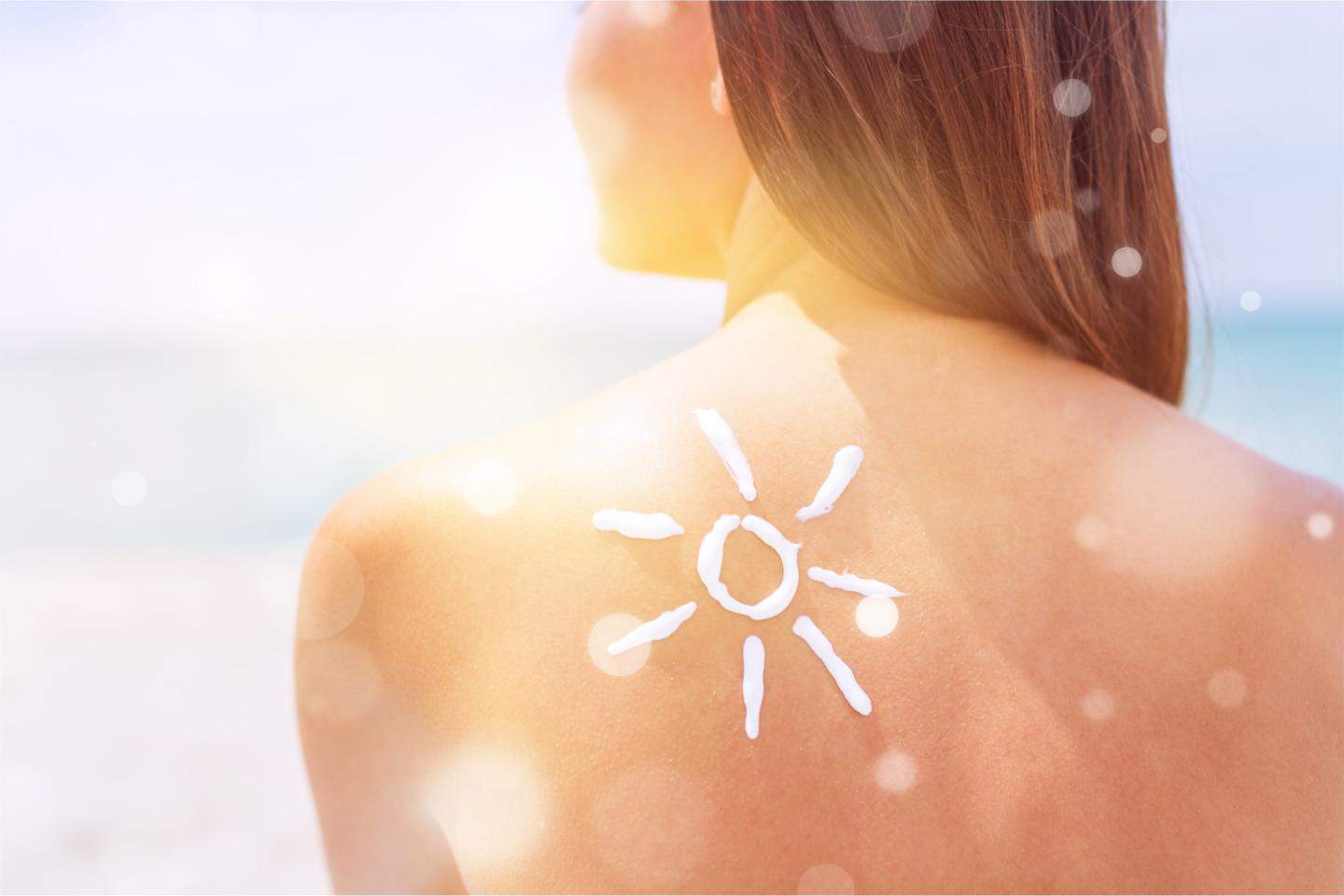 Woman with Sun Cream on her back over ocean background - holiday toiletries