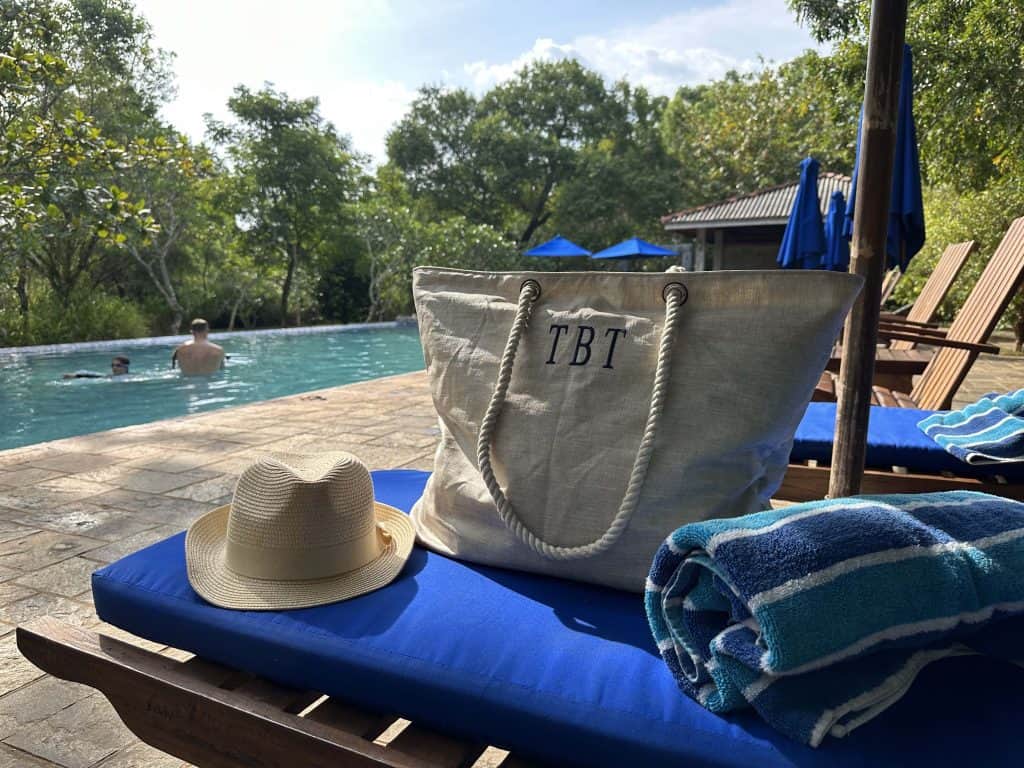 Beach bag, hat and towel on a sun bed with a pool in the background