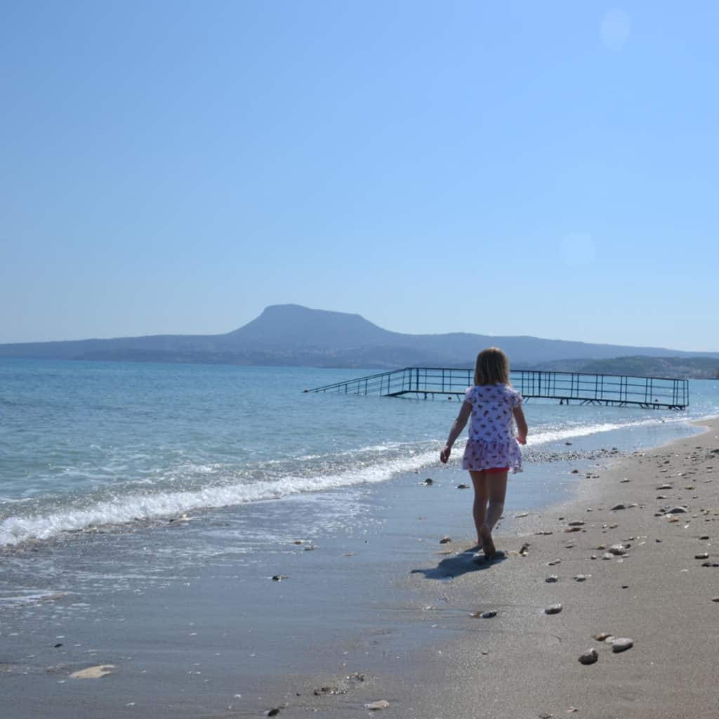 Tin Box Tot walking along sandy beach in Crete