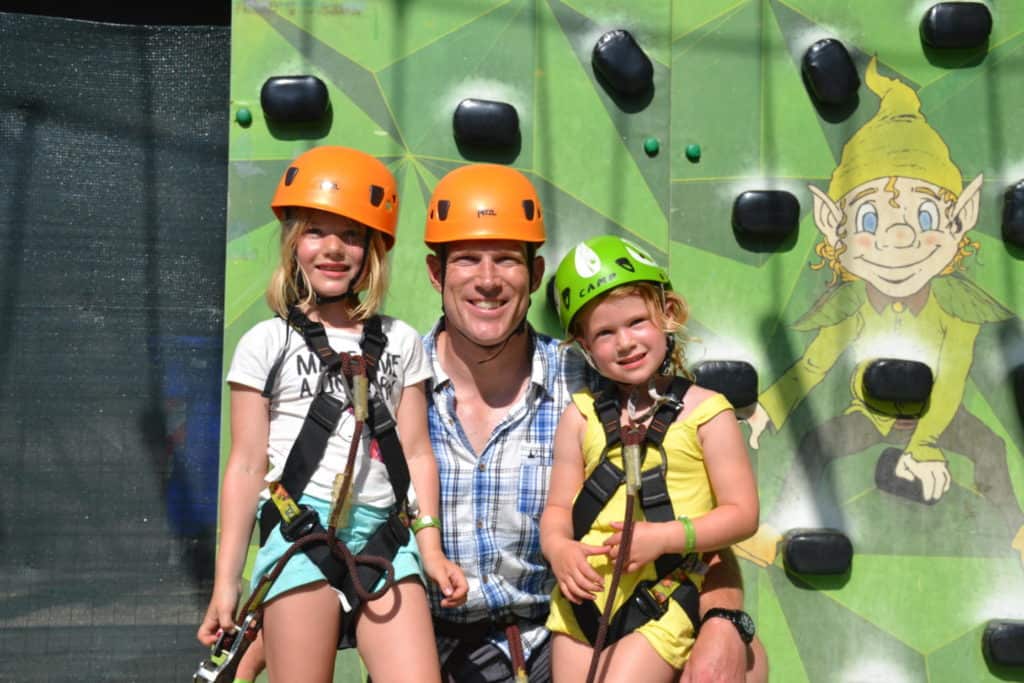 Mr Tin Box, Tot and Baby wearing climbing gear in front of climbing wall