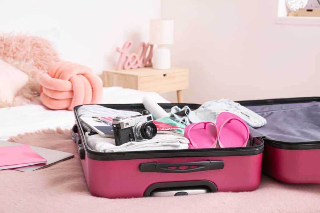 Open suitcase with packed clothes and accessories on bed - what to pack for a Caribbean cruise