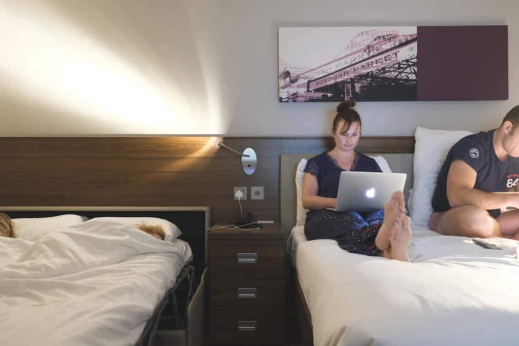 Claire working on laptop in the next bed to sleeping kids in hotel room