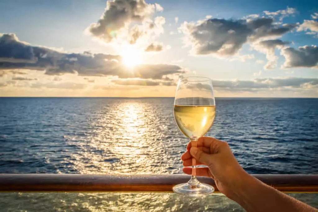 Glass of wine being held up in front of sunset at sea