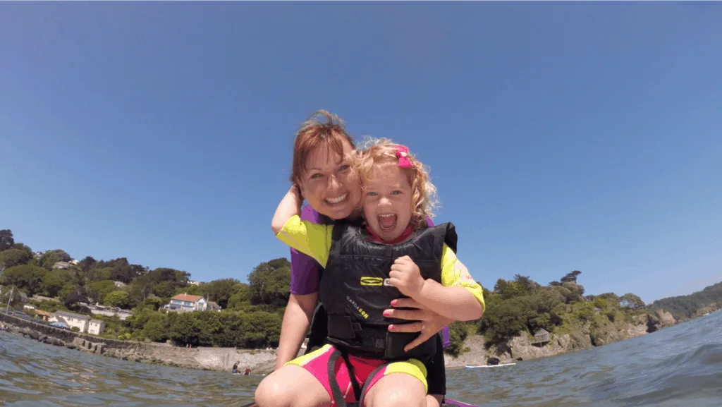 Mum and girl on paddle board. Girl wears a Gul buoyancy aid