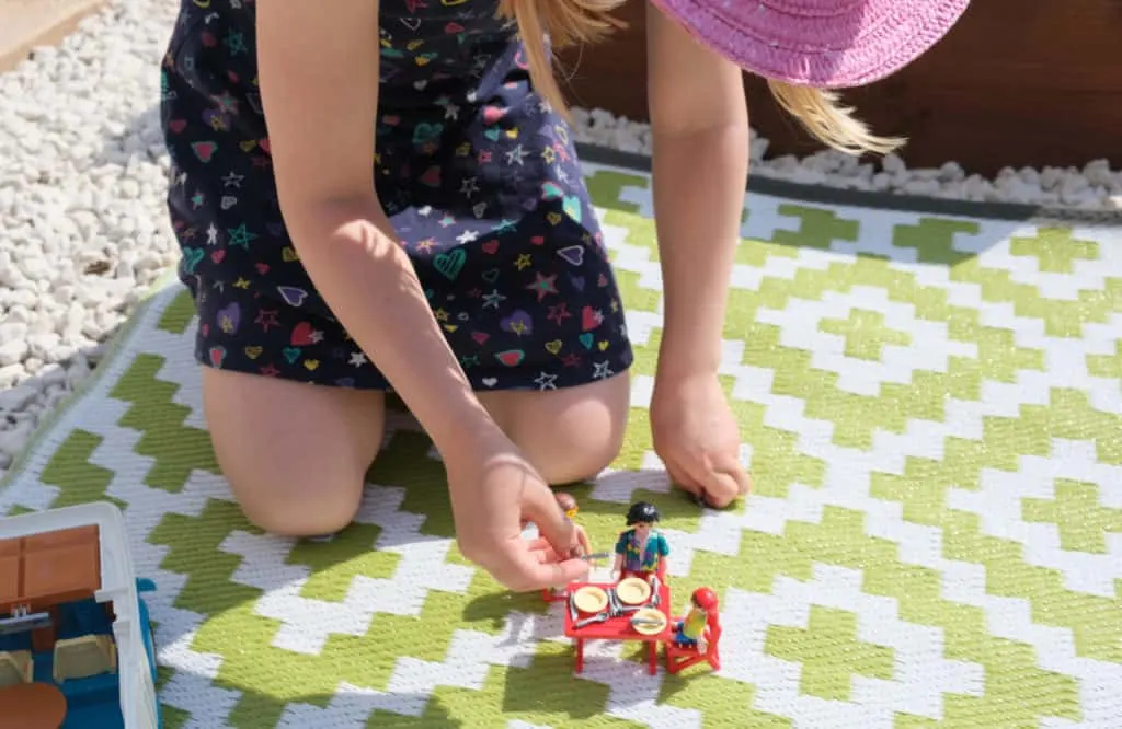 Child plays with PLAYMOBIL figures on mat in garden
