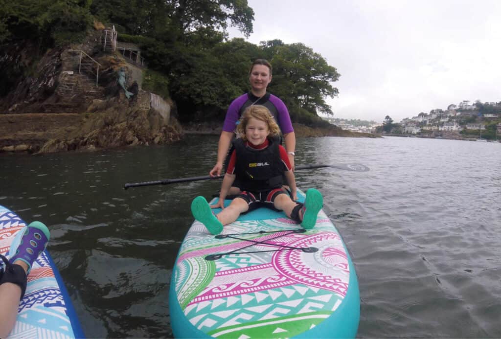 Mum and daughter sitting on SUP board on river