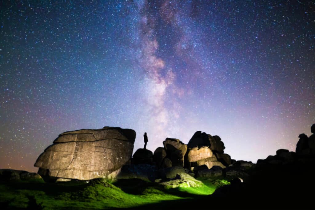 Person standing on tor on starry night on Dartmoor National Park in Devon