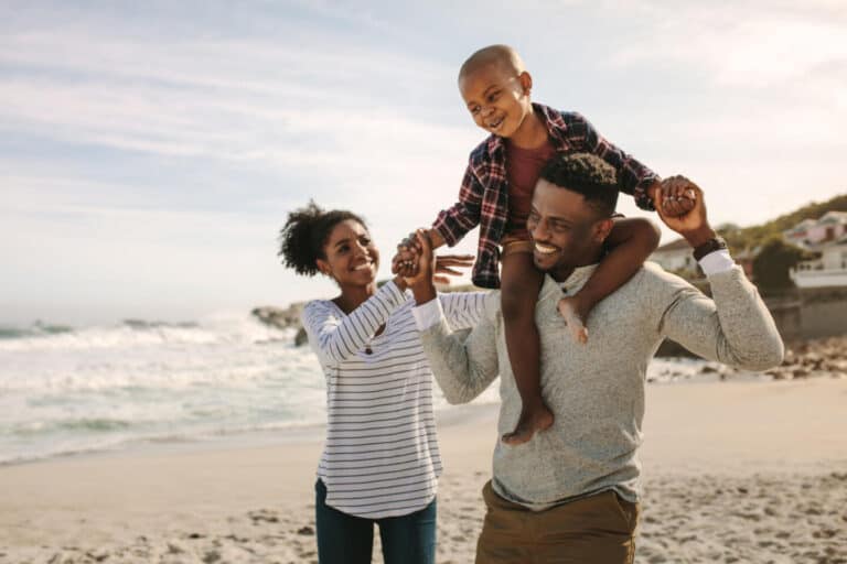 Parents carrying son on shoulders on beach vacation.