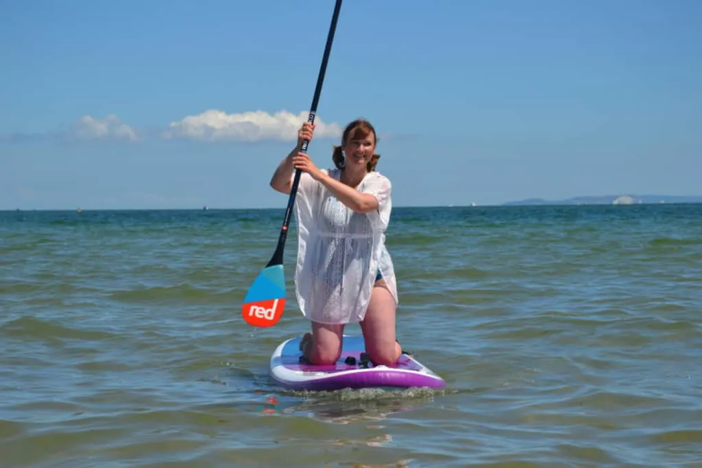 Claire kneeling on paddle board in the sea