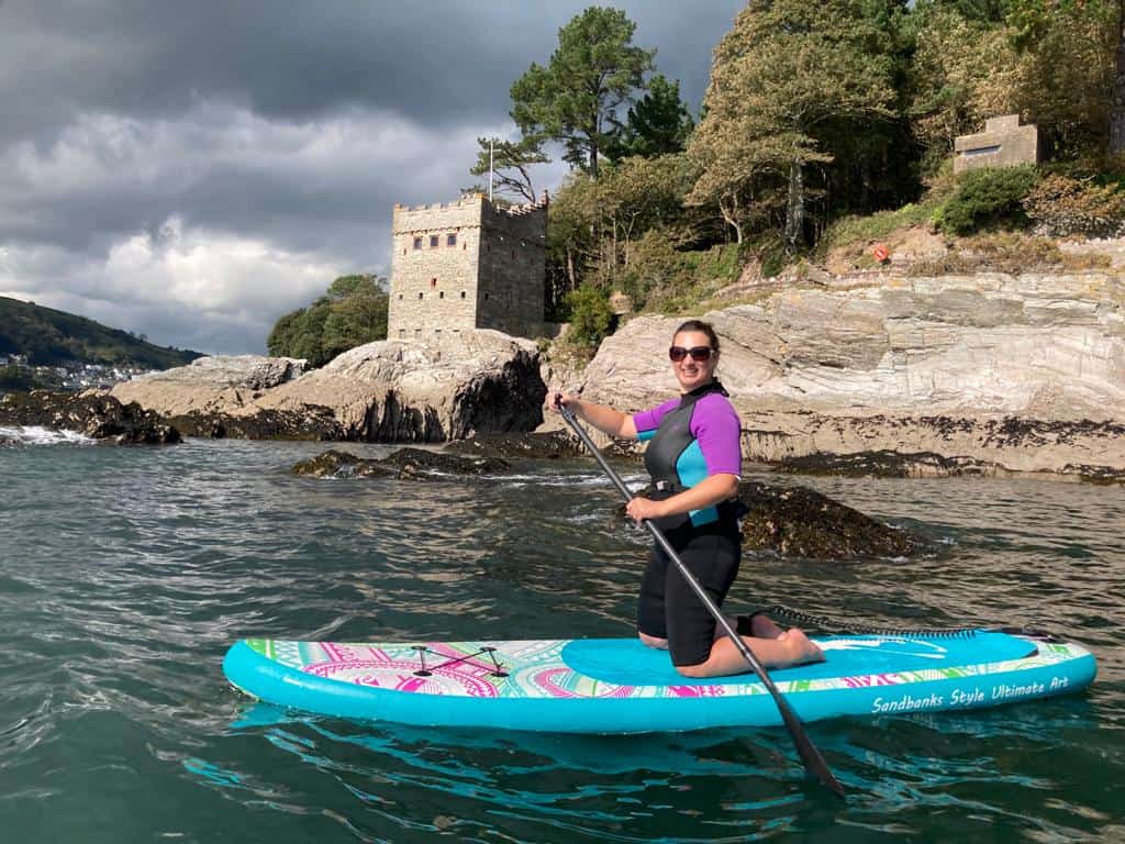 Claire kneeling on paddle board on the sea in front of Kingswear Castle in Devon