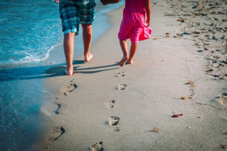 father and daughter walking on beach leaving footprint in sand