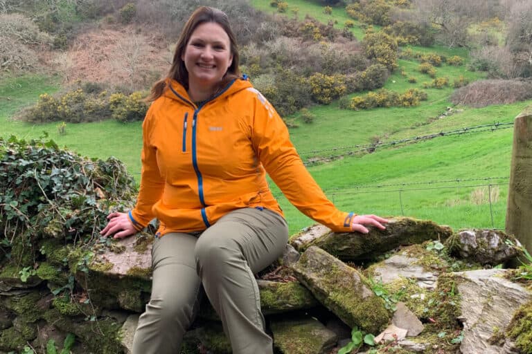 Claire sitting on dry stone wall in countryside wearing Keela Women's Machu Trousers