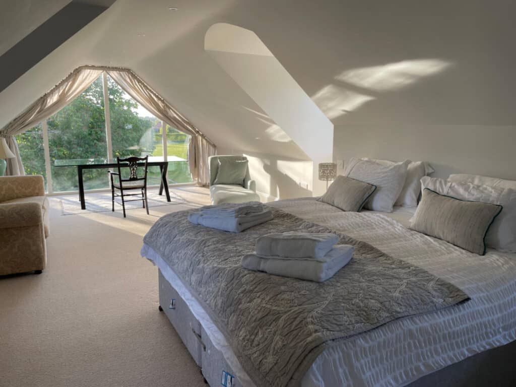 Master bedroom with bed and desk in front of glass wall looking out onto garden and countryside