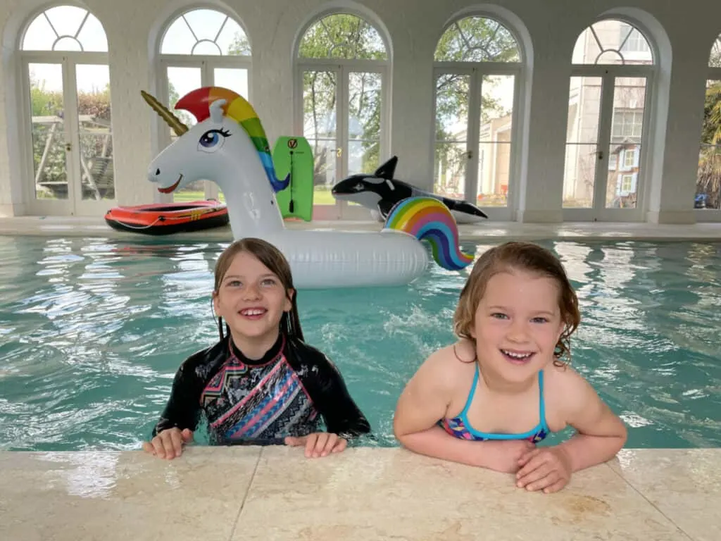 Children propped on the side of swimming pool with large inflatables behind them