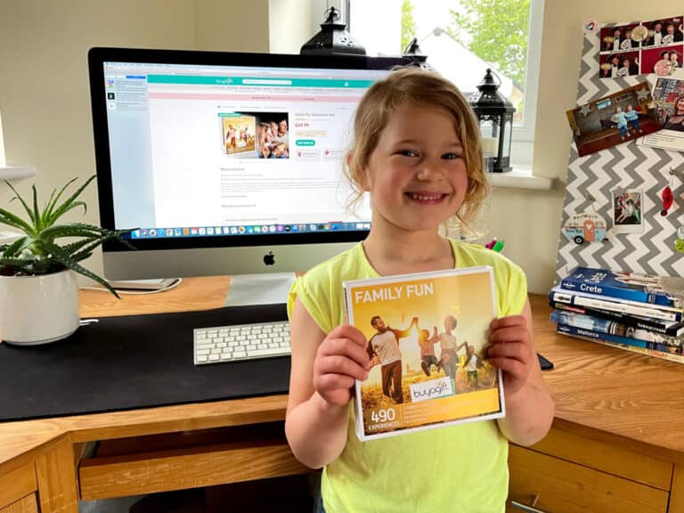Child holding Buyagift box at desk in front of Mac computer