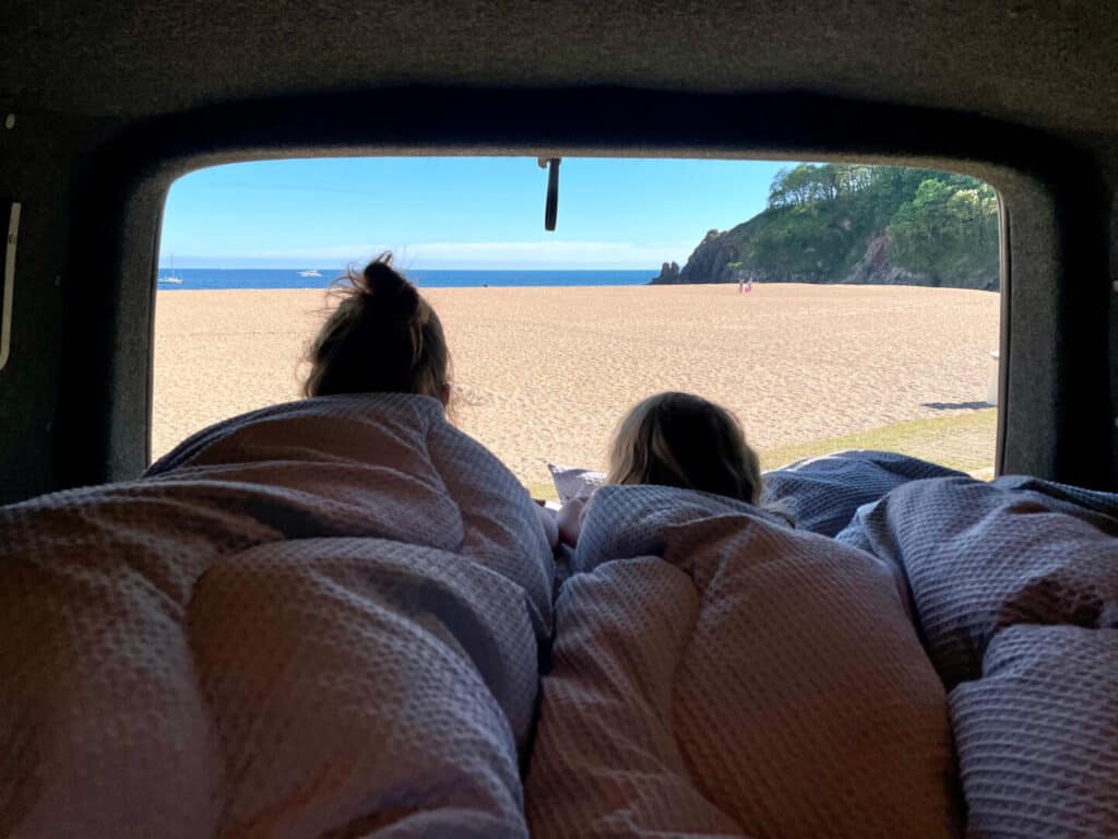 Mum and child looking out the back of camper van a a view of a beach