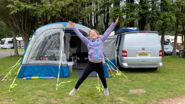 Tot doing a star jump in front of camper van awning