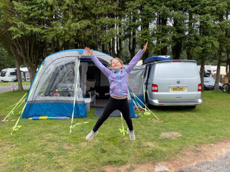 Tot doing a star jump in front of camper van awning