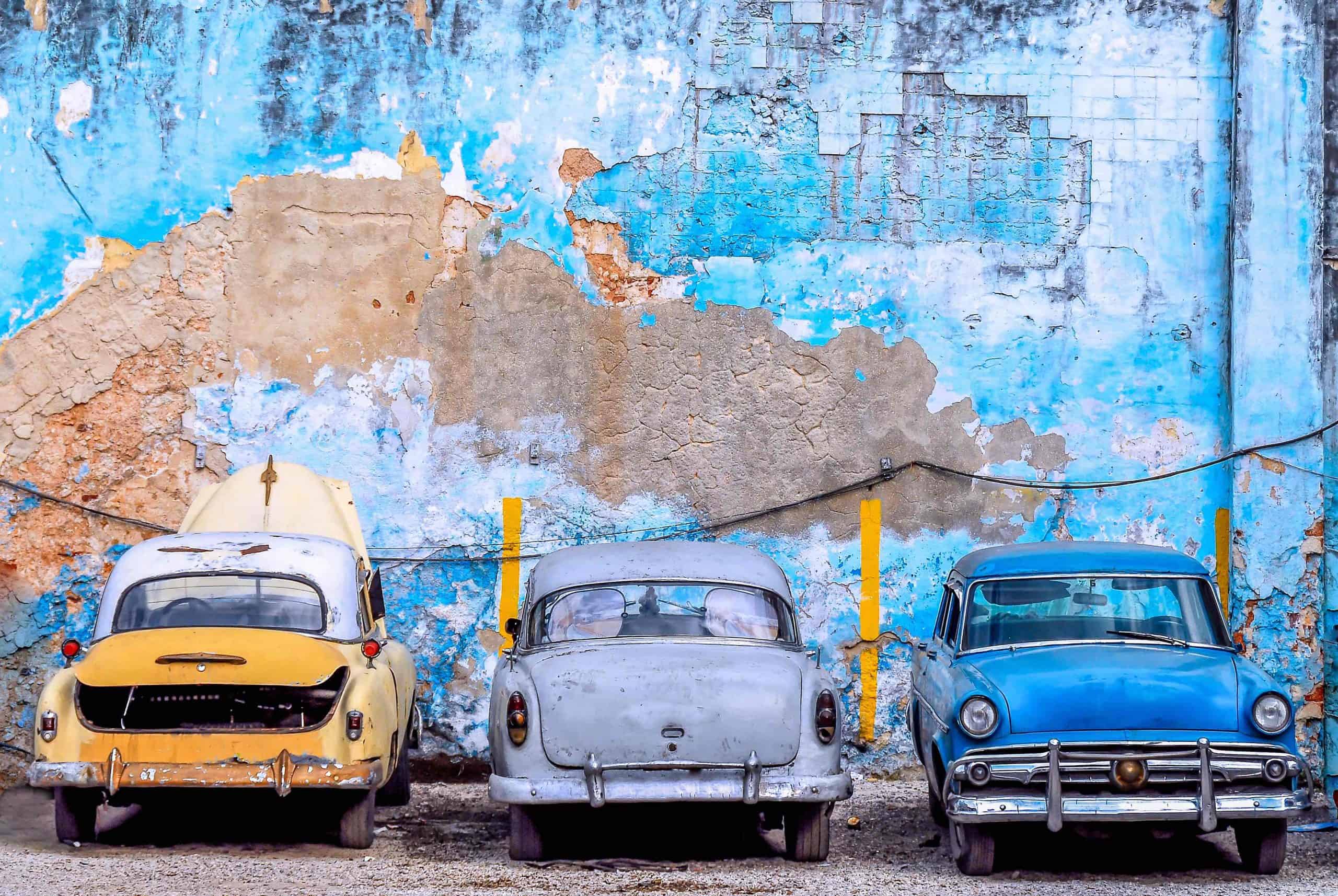 Three colourful Cuban cards agains a peeling blue painted wall