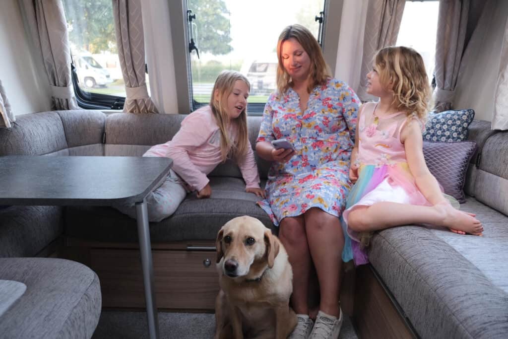 Claire and girls looking at phone screen while sat in caravan lounge