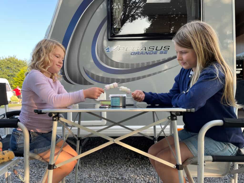 Children sat at table outside caravan toasting marshmallows on small burner