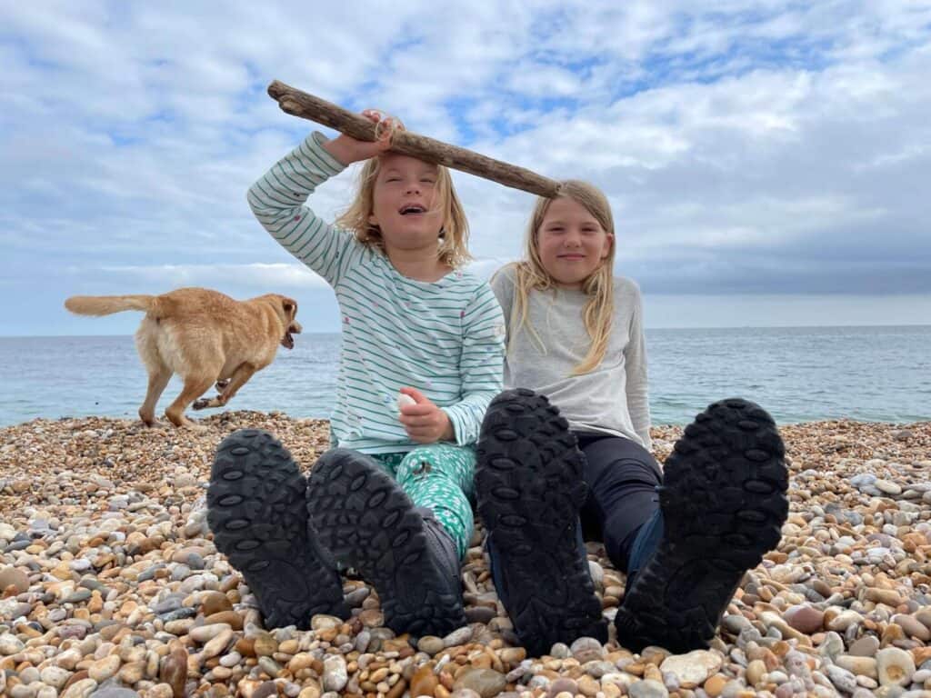 Girls sat on the beach with a dog running in the background