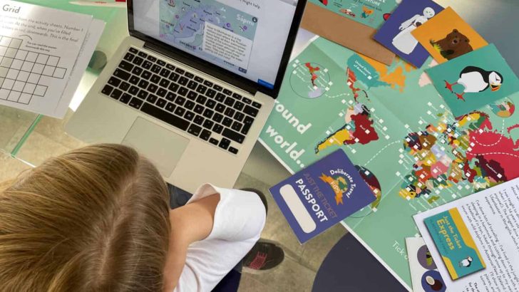Child sat at laptop with work sheets, map and passport from Just The Ticket