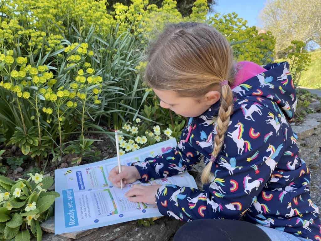 Girl crouched down in garden pencilling information onto a National Trust Easter Trail sheet