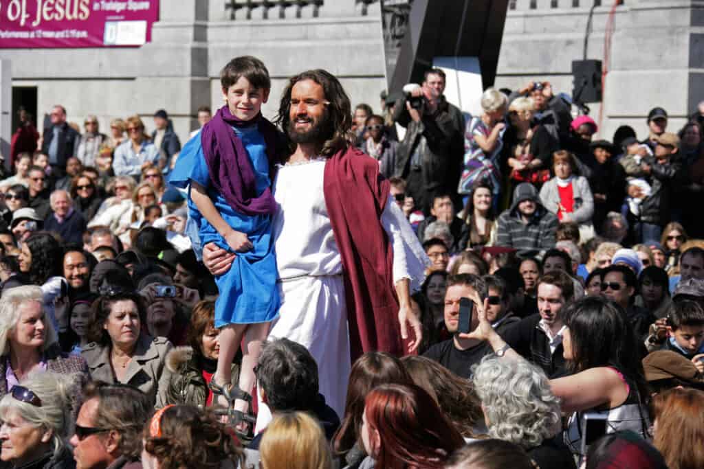 Actor playing Jesus carrying young child through crowd