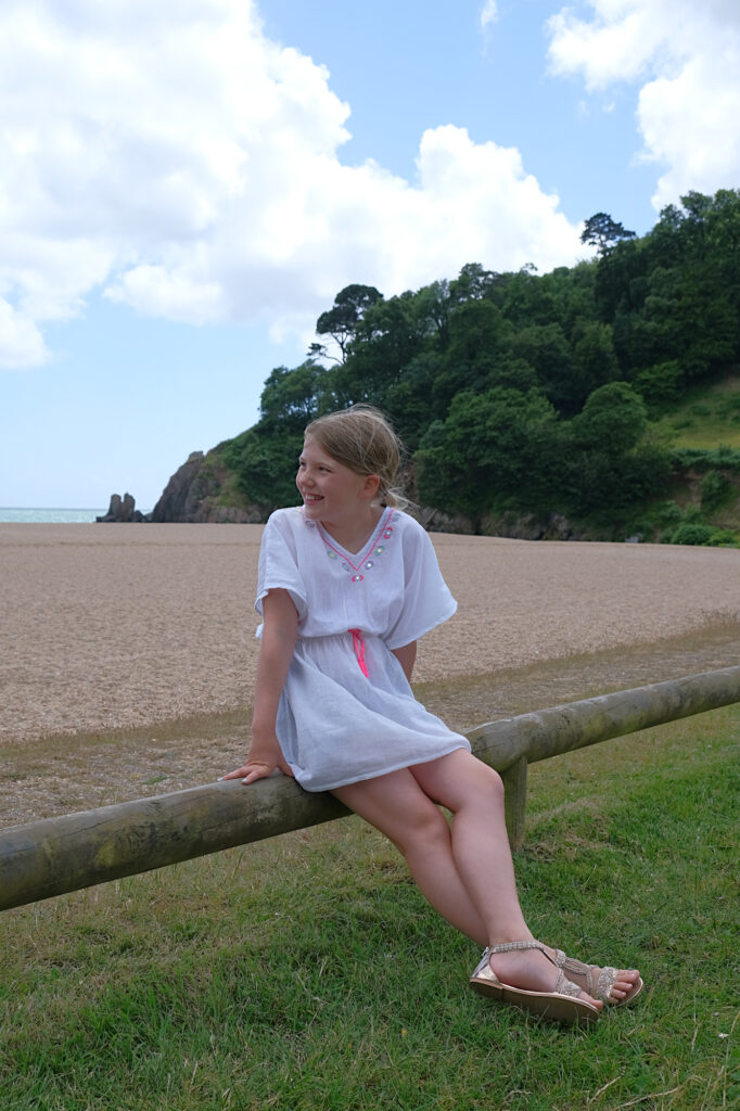 Girl sat on wooden fence in front of beach
