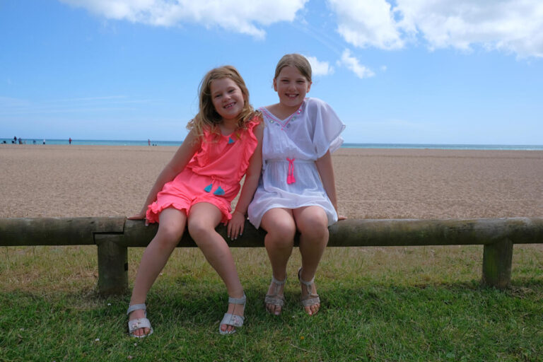 Girls sat on wooden fence in front of beach