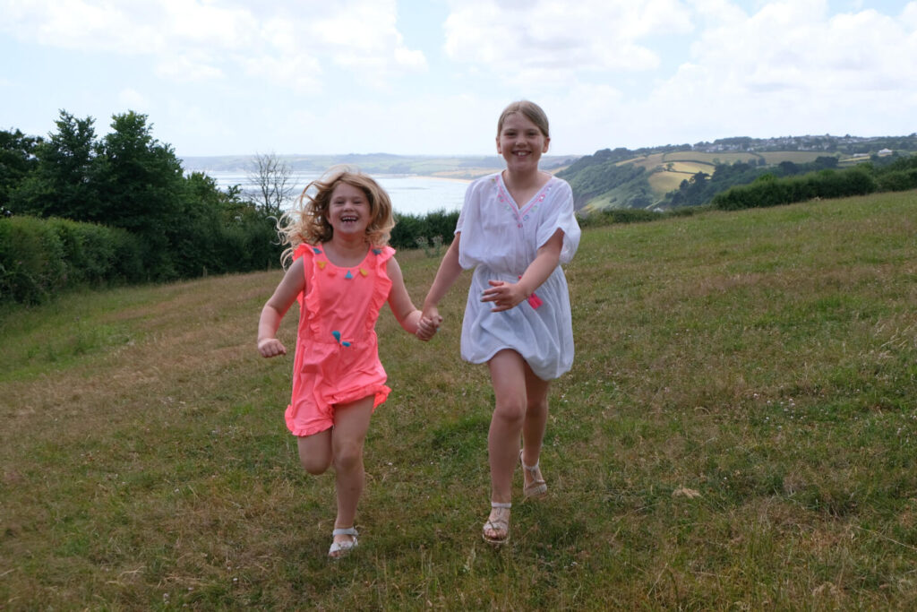 Two girls running towards camera in summer clothes with coast view behind