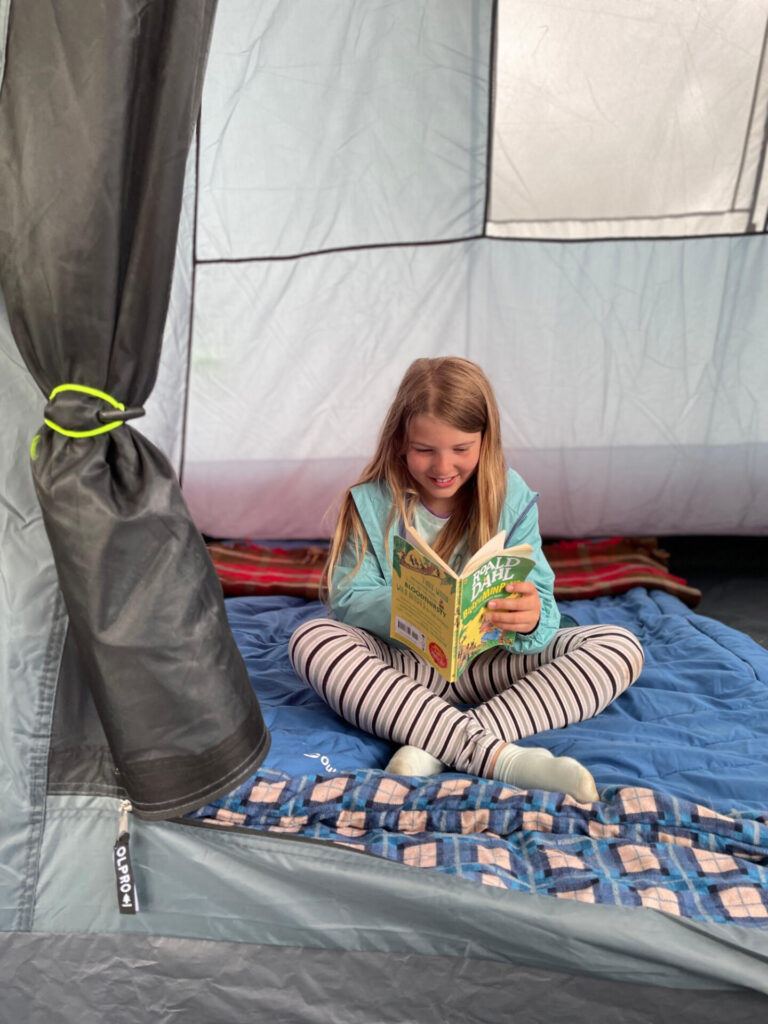 Child reading a book cross legged on a sleeping bag in tent