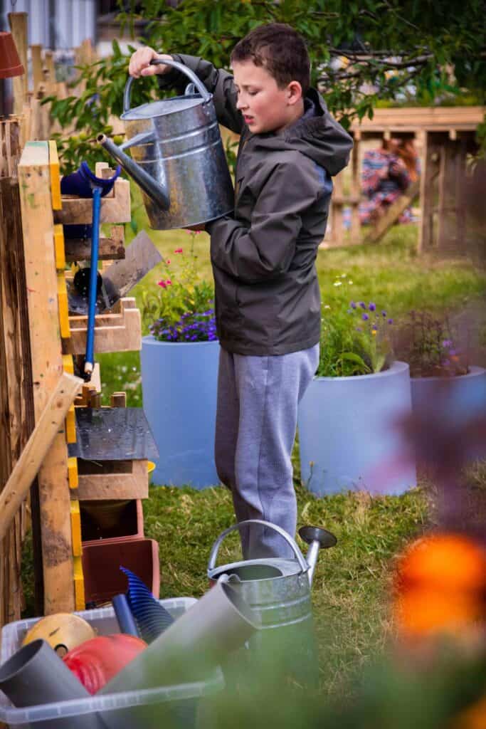 Boy watering plants in garden play space