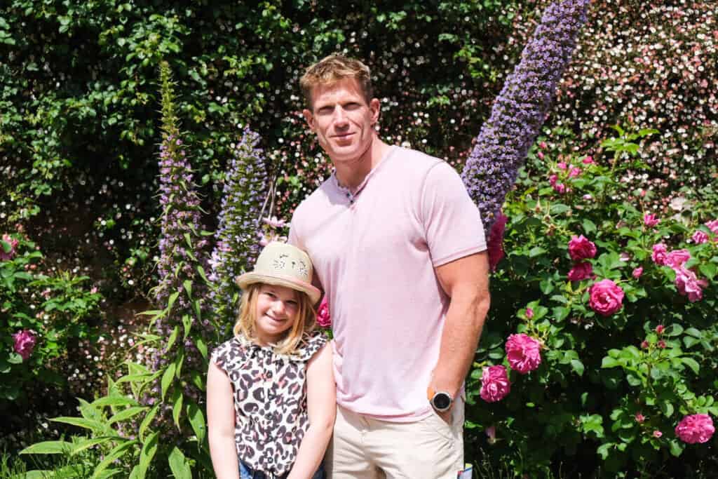 Father and daughter pose in front of flower beds at Jersey Zoo