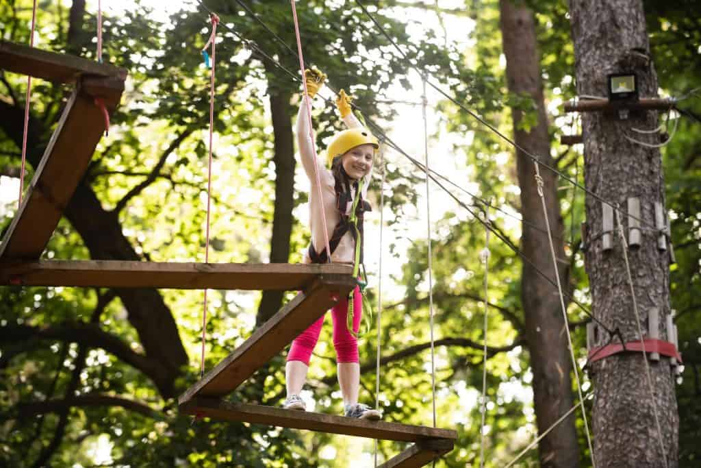 Happy Little girl climbing a tree. Go Ape Adventure. Hike and kids concept. Cute little girl in climbing safety equipment in a tree house or in a rope park climbs the rope