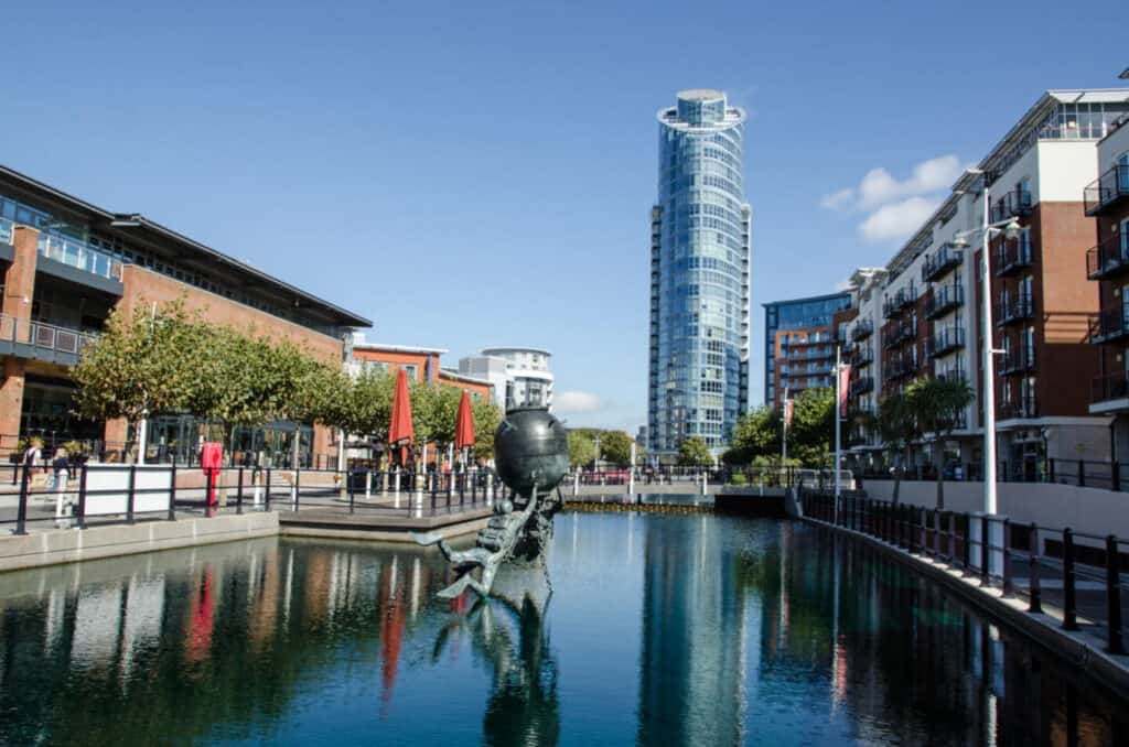 View along one of the converted docks at Gunwharf Quays, Portsmouth with the Vernon Monument to Royal Navy divers and bomb disposal operatives.