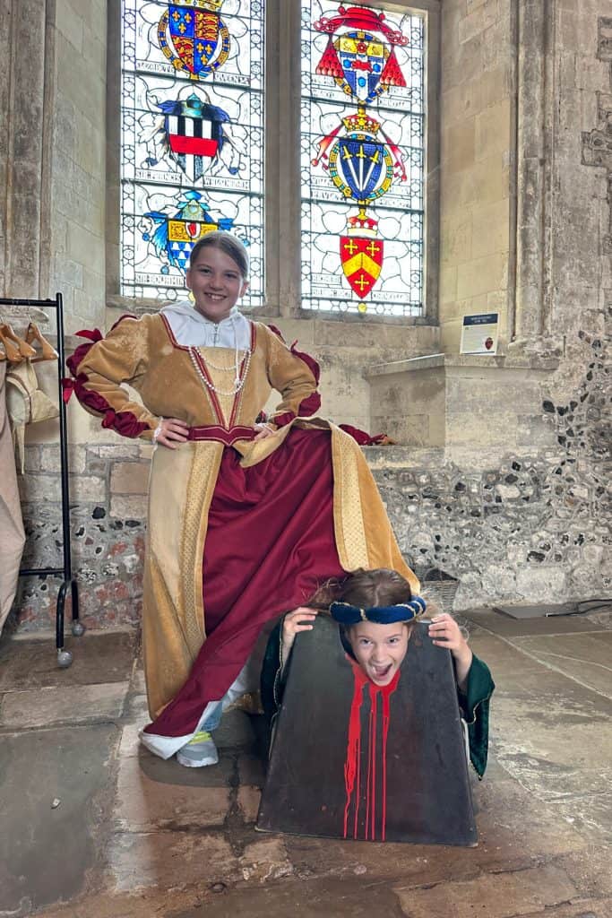 My daughters dressed in Tudor costumes. My youngest is knelt with her head in a chopping block and my eldest has her foot on her back. They are play acting