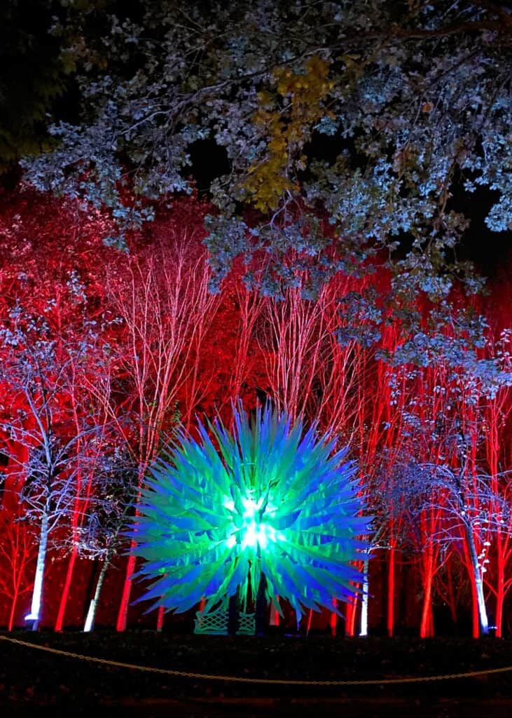 A forest backdrop illuminated in red lights with a giant orb light fixture aglow in blue and green