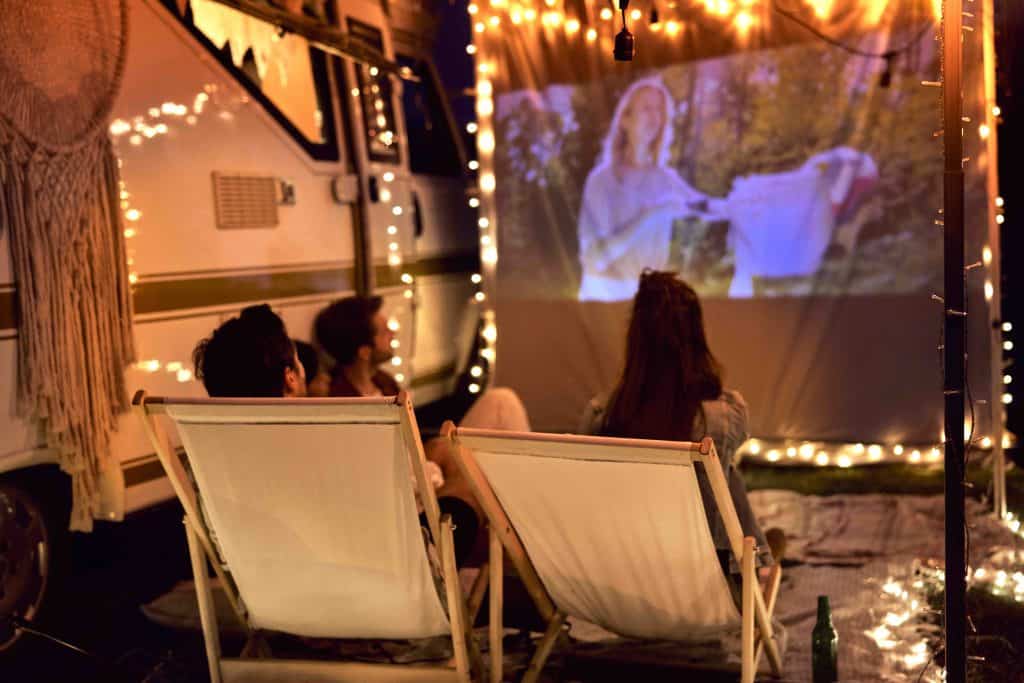 Cheerful people watching a movie projected onto a sheet on camping site